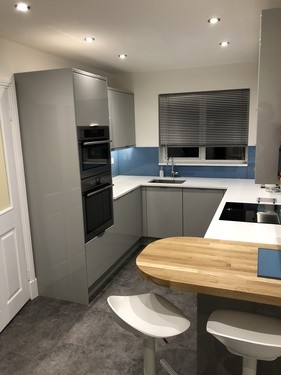 Grey U-shaped kitchen with wooden breakfast bar and blue splashback