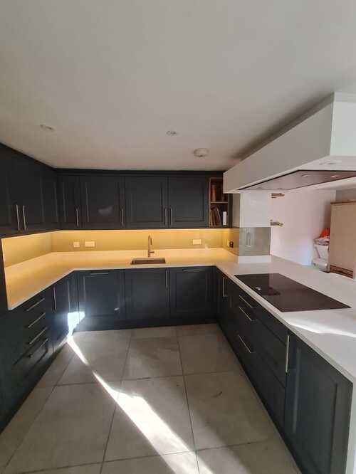 Modern kitchen with dark cabinets, white counters, and yellow LED underlighting