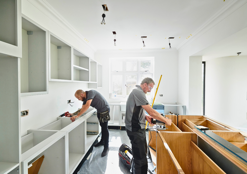 Two workers installing white kitchen cabinets in a modern kitchen renovation