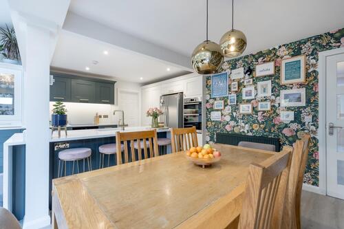 Kitchen-diner with floral wallpaper, brass pendants, and wooden table