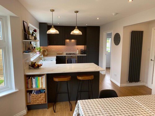 Dark kitchen with white island, pendant lights, and wooden bar stools