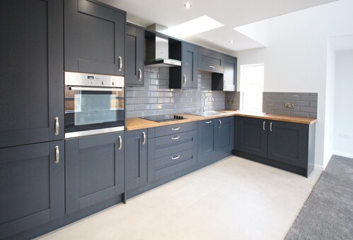 White kitchen cabinets with wooden countertops and grey tile backsplash