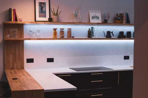 A black kitchen with pale worktops, gold handles and wooden accents