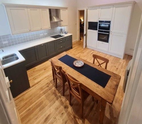 Two-tone kitchen with dark base units, white wall cabinets and wooden dining table