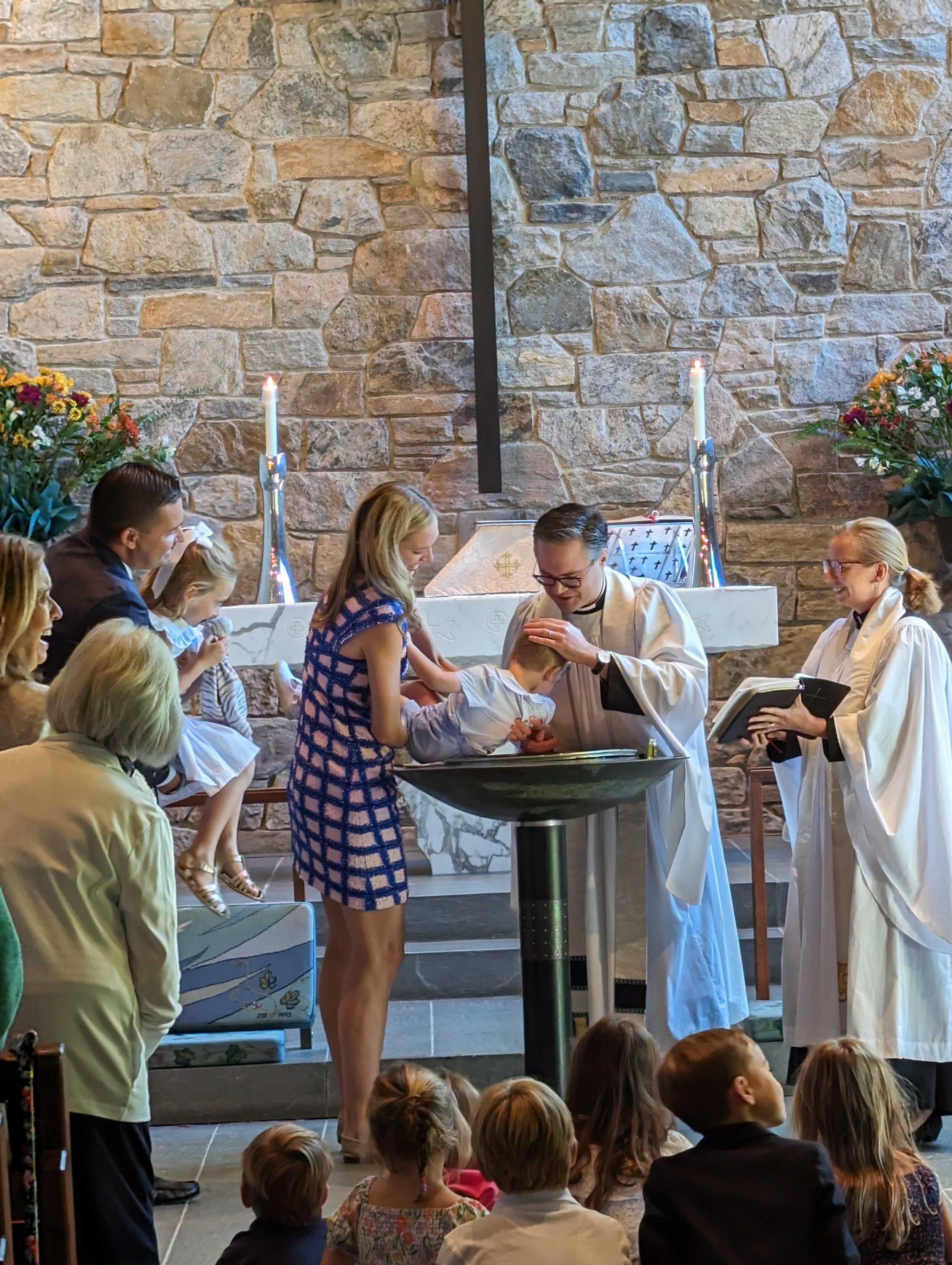 A child being baptized at St. Barnabas, surrounded by family at the font