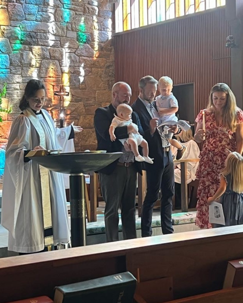 Families and clergy gathered around the baptismal font at St. Barnabas