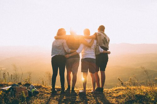 Clean Group small group of friends with their back to the camera while standing on a mountainside facing the sun in late afternoon.