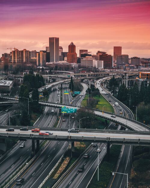 Overhead drone view of Portland, Oregon cityscape and highway system with buildings and pink & purple sky in the background for The Clean Life Mission & Vision page.