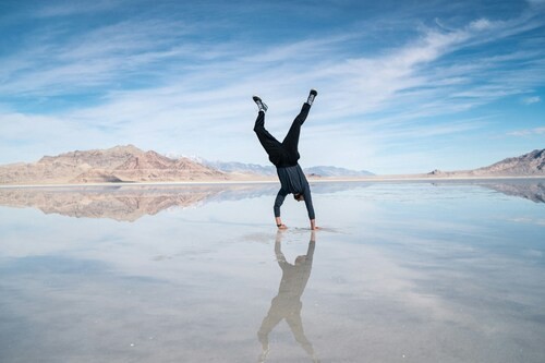 A man doing a handstand outdoors over a wet, reflective surface with blue skies and mountains behind him. Image for The Clean Life's welcome blog post about addiction recovery and recovery resources.