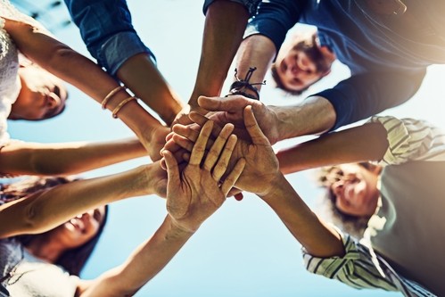 Clean Recovery, addiction recovery, trauma recovery, a community of people standing in a circle with their hands all together inside the circle, shot from below their hands looking up at their hands and smiling faces.