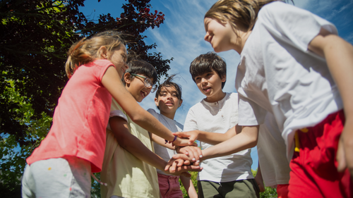 Image of five children standing in a circle with their hands in the middle staked one on top of the other.