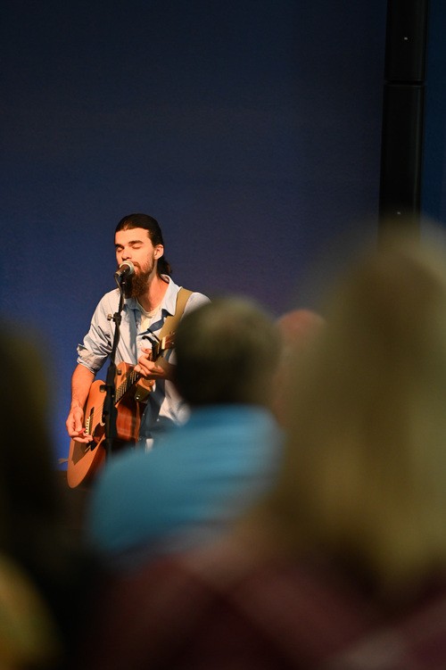 Man singing into a mic and playing a guitar