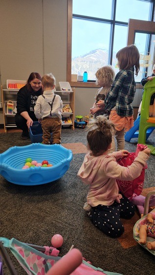 A Christ Center Kids volunteer playing with toddlers around a ball pit