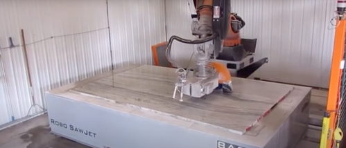 Industrial sawjet machine cutting a large stone slab in a workshop.