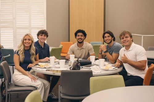 Group of college kids sit at table eating lunch.