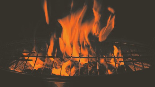 Flames rising from a charcoal grill representing the Bullets and Sausage college outreach cookout event at UHBC in Stillwater, Oklahoma