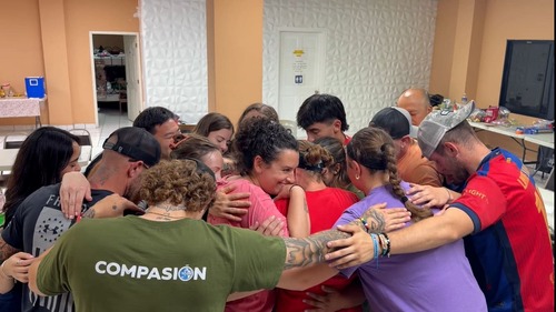 A circle of linked arms surrounds local coworkers at the center, heads bowed together in prayer. 短宣队员手臂相扣围成一圈,当地同工站在圈中心,大家低头一同祷告