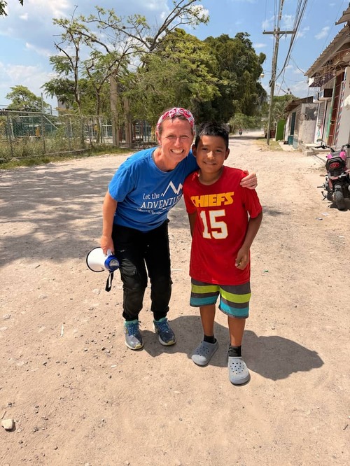 Pastor Andrea with a big smile and half squatted down holding a megaphone puts her arm on a little Honduran boy Andrea 牧师半蹲面带微笑,手拿扩音器与洪都拉斯孩子合影