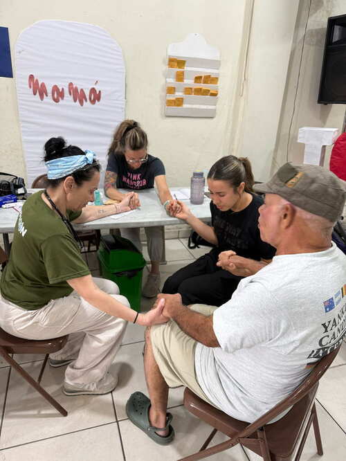 Justine and others, eyes closed, hold one another's hands in prayer. Justine和其他人，闭着眼，手拉手同心祷告。
