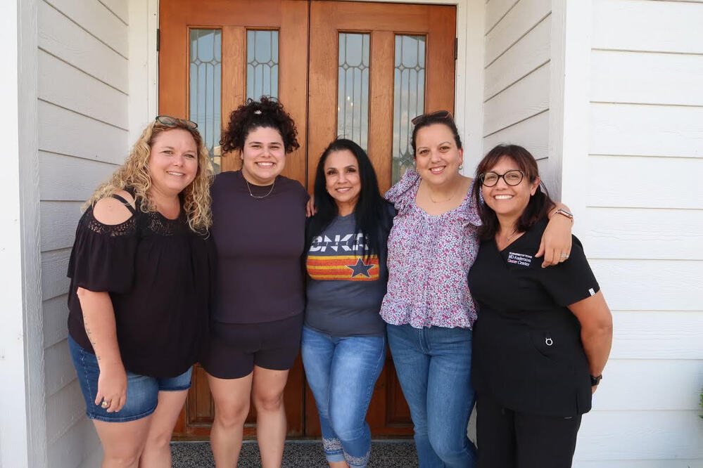 Five women smiling together outside a home