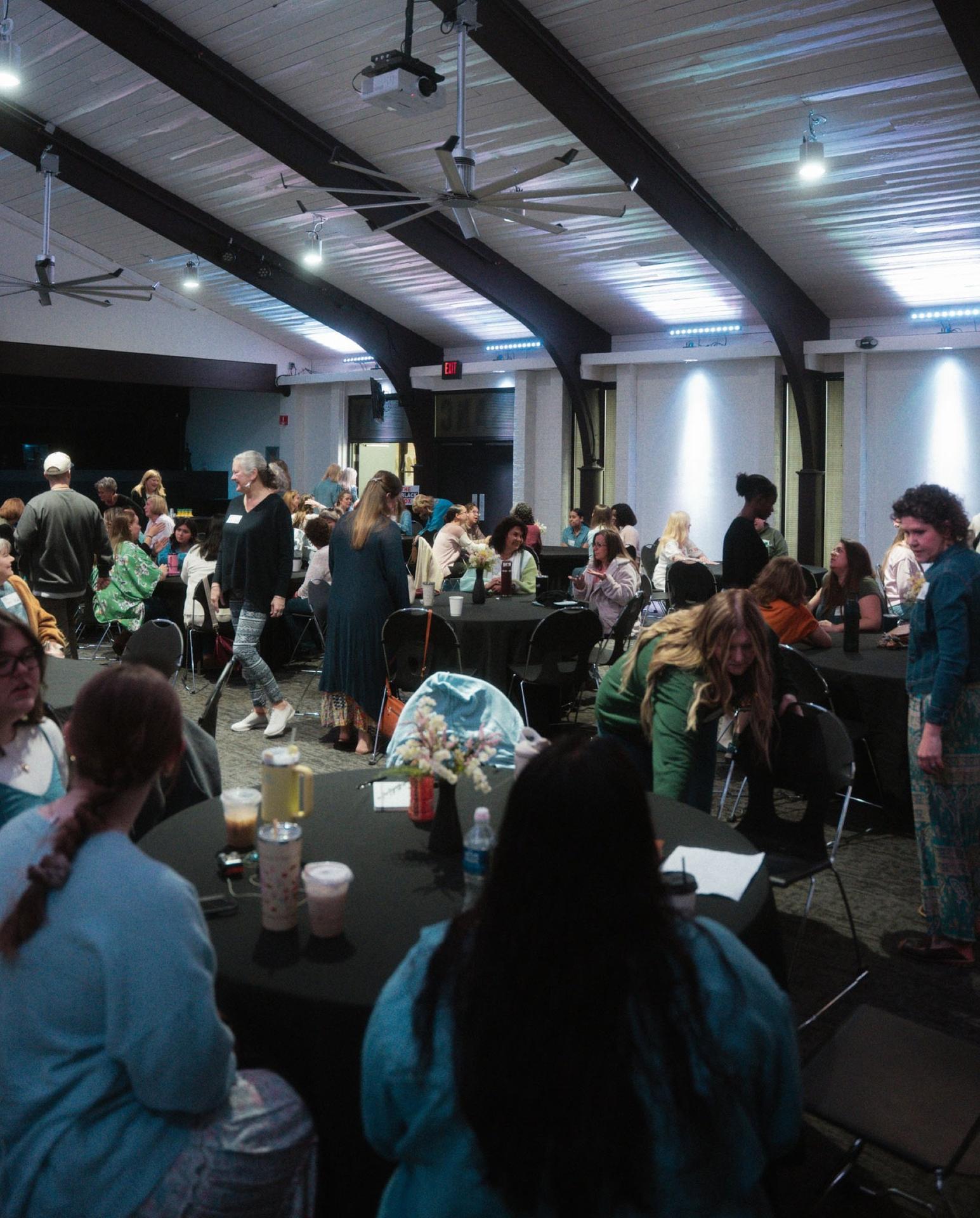 A full room of women talking and mingling around round tables