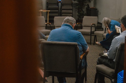 Small group gathered in a circle for Sunday morning prayer meeting as viewed through a doorway.