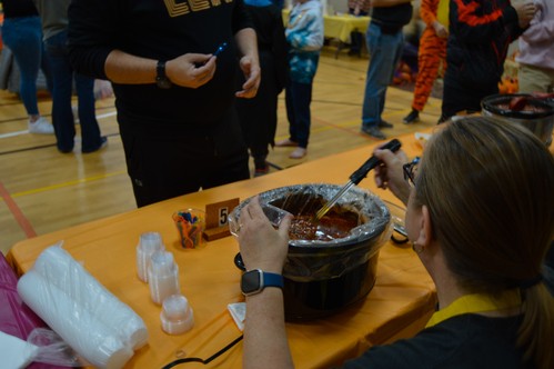 A woman serving chili from a crockpot with multiple people visible in the background
