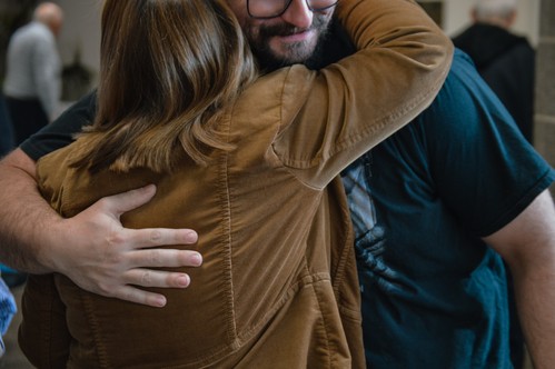 A younger man and older woman embrace in the church lobby before Sunday service begins.