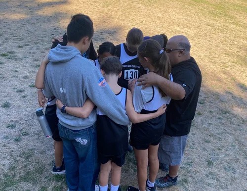 Mr. Gaeta with Heritage cross-country athletes gathered in prayer before a race