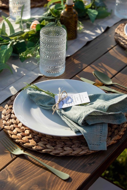 A sage linen napkin tied with twine and rosemary at an individual place setting
