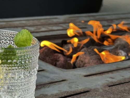 A textured glass beside the warm flames of a patio fire table