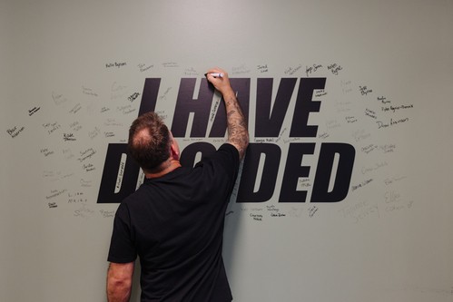 Ben signing his name on a green wall that says 