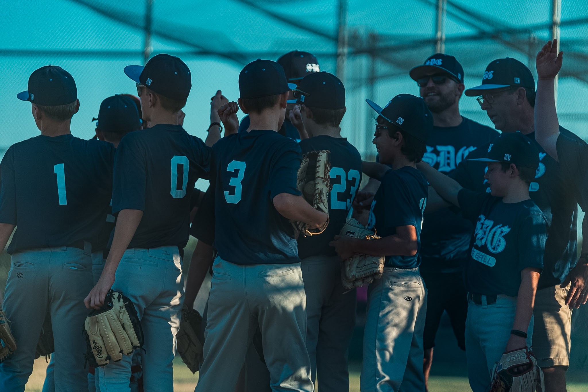 SDG Baseball players and coaches bringing their hands together in a team huddle
