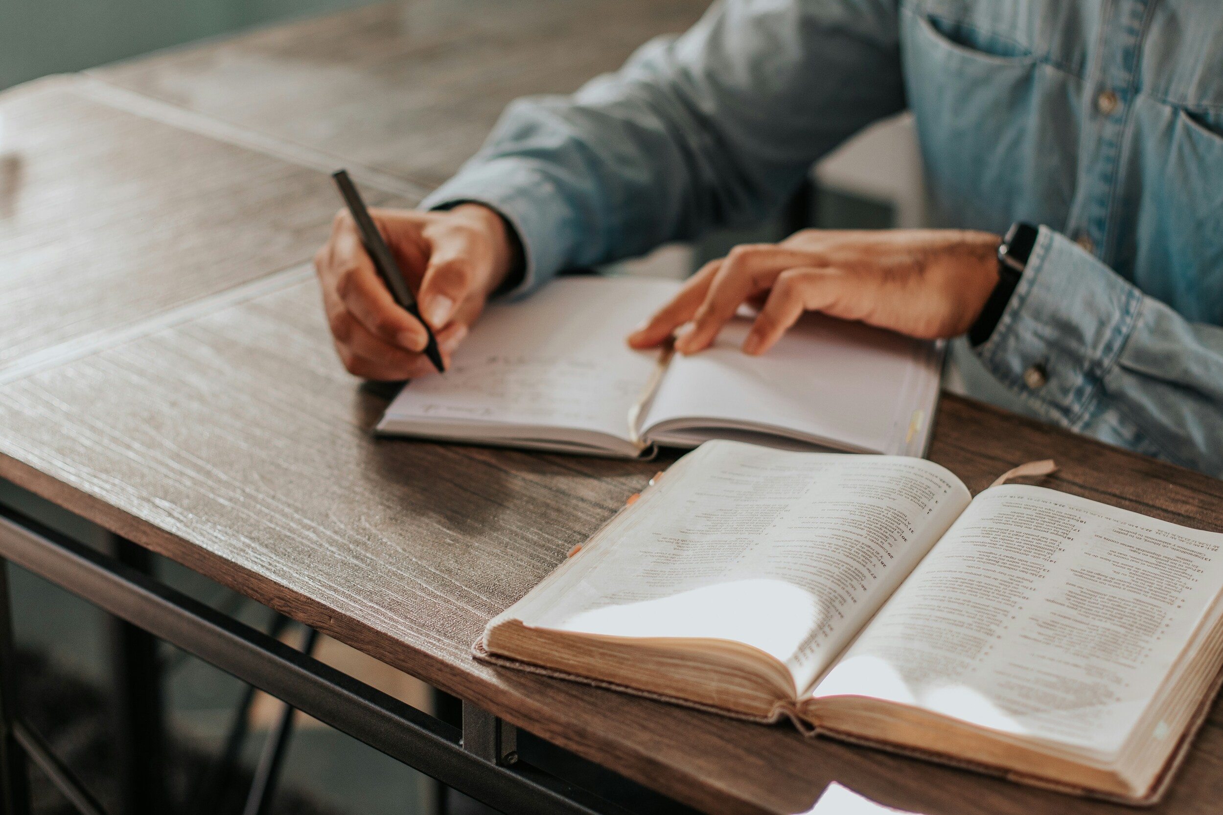 A person studying and taking notes beside an open Bible