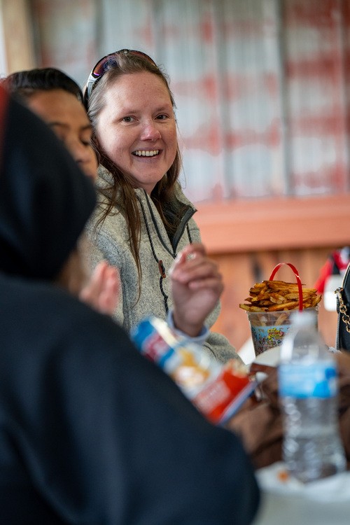 two ladies smiling while holding plates of food with flags of different countries hanging behind and above them