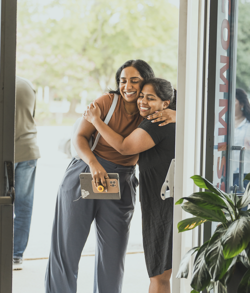Two women hugging at the entrance of Commission Church in Plano TX, welcoming each other in a non-denominational spirit-filled community.
