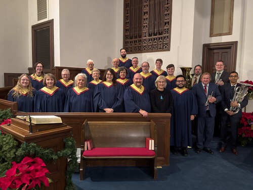 An image of several members of the church choir, all dressed in navy blue robes with white trim, singing in Sunday worship in the sanctuary.
