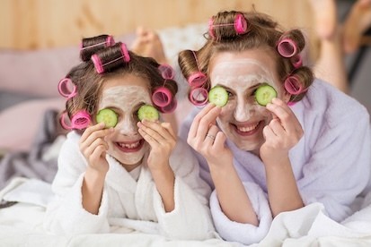 A mom and daughter wearing face masks and hair rollers, smiling together during a playful at-home spa day.