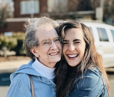 An older woman and a younger woman smiling and hugging outdoors, celebrating their close bond.