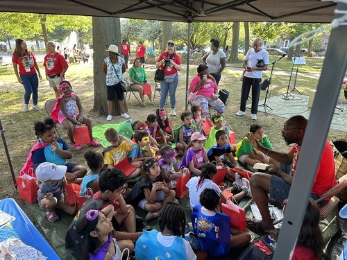 VBS leader teaching a Bible story at a themed station while children listen and participate.