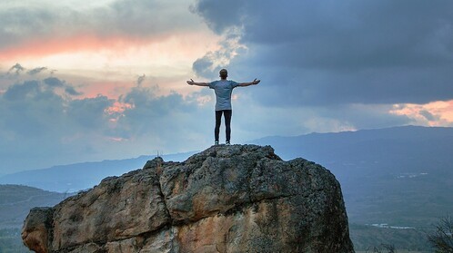 man on top of mountain with outstretched arms