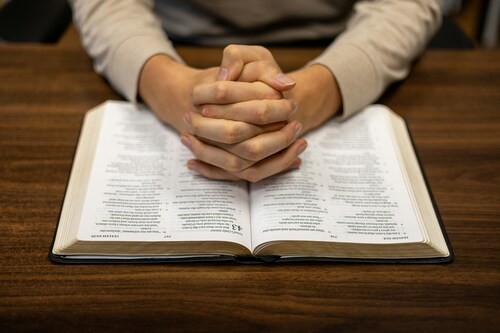 hands folded in prayer over an open Bible