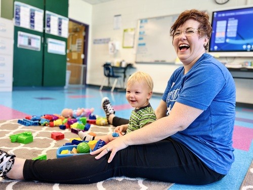 Smiling RCC Kids volunteer playing with a toddler on the classroom floor during Sunday service.