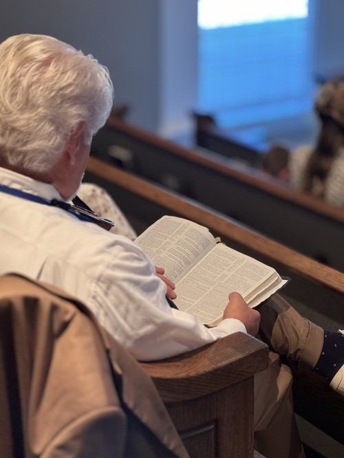 man reading Bible in church pew