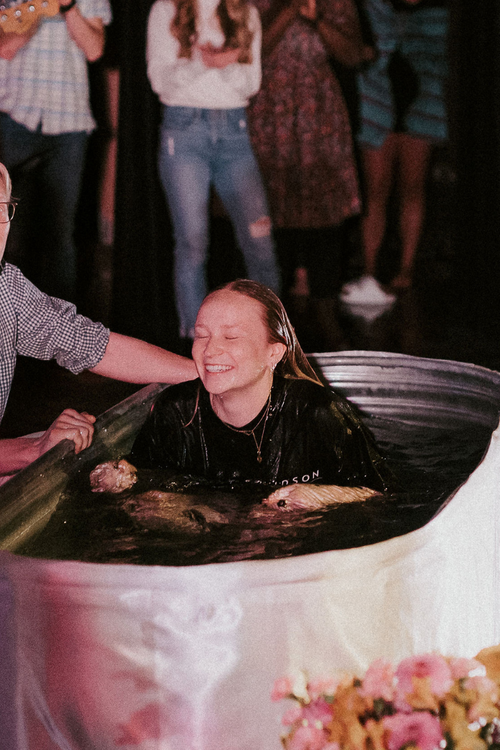 woman smiling and sitting up in a tub of water after being baptized