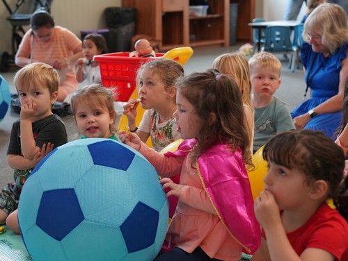 Preschool children ages 2-4 sitting together, playing and holding a large soccer ball during church program.