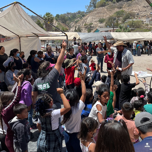 crowd of children raising hands and a speaker with his hand raised
