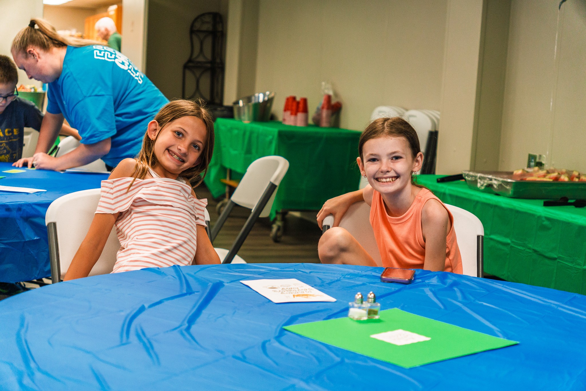Two girls smiling at a table during a kids event