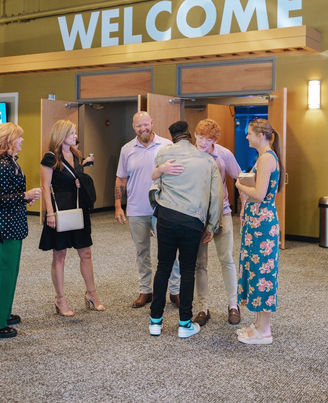 Friends hugging and laughing under the WELCOME sign at the Tucker auditorium doors