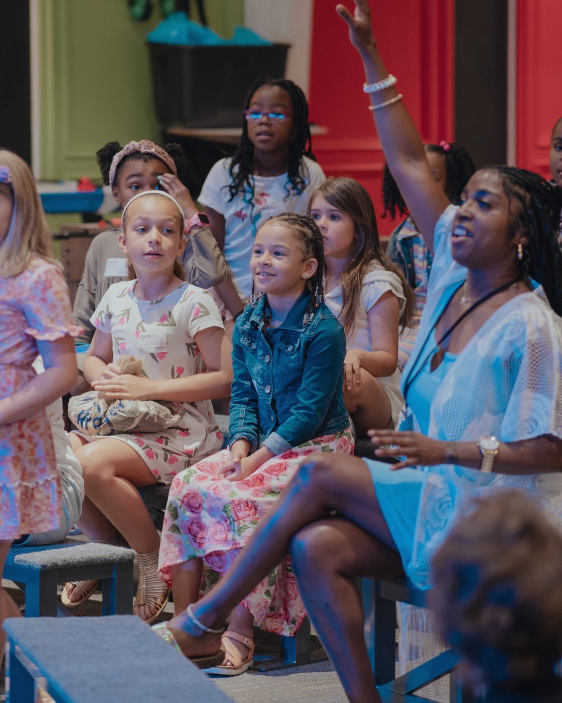 An MW Kids leader cheering with a room full of kids on their benches